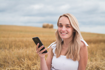 beautiful young woman in a mown wheat field with a phone in her hands