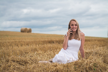 beautiful young woman in a mown wheat field with a phone in her hands