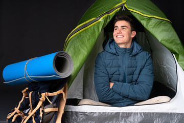 Teenager caucasian man inside a camping green tent isolated on black background happy and smiling
