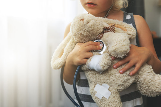 child playing doctor with soft toy. girl examining bunny with stethoscope at home
