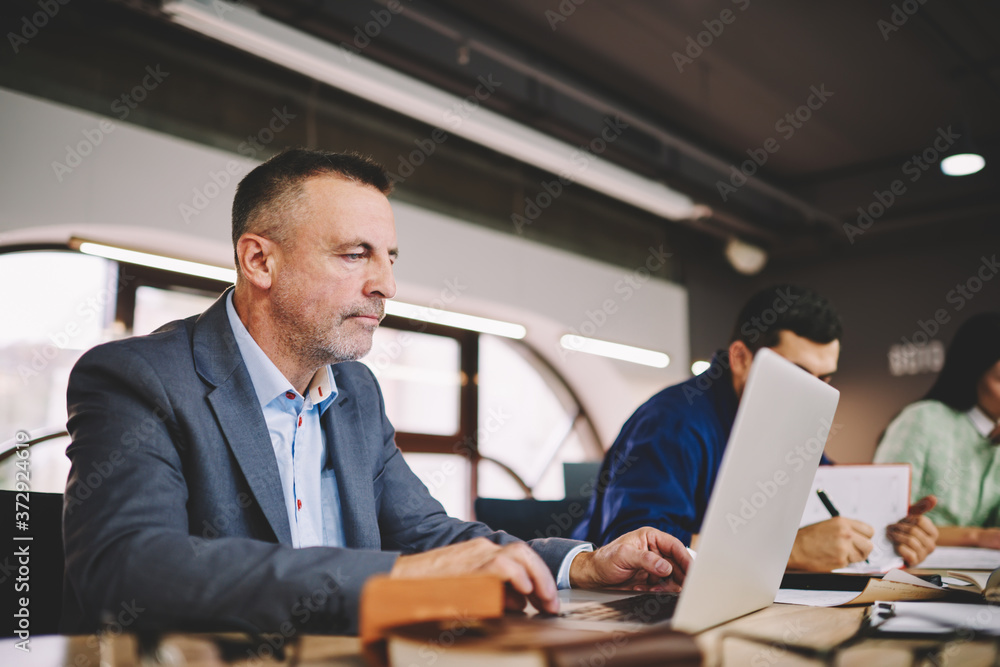 Aufkleber concentrated mature man in formal clothing sitting at modern macbook computer connecting to wireless