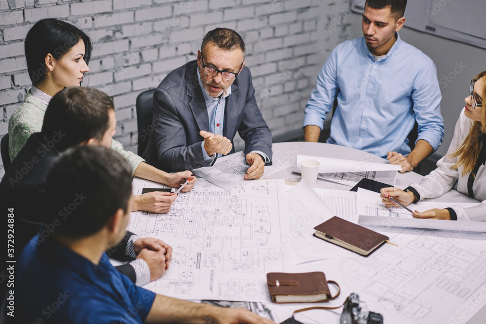 Poster successful mature director of building company in eyeglasses explaining tasks of new architectural p