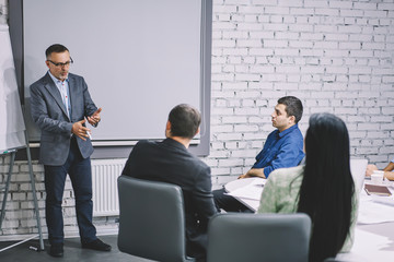 Professional coach dressed in formal clothing conducting productive workshop about important business tasks of collaboration to group of engineers.Mock up area for your advertising text message