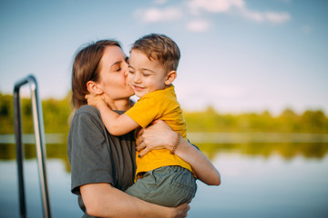 Mother kiss and hug son on dock on nature background. Summer photography for blog or advertising...