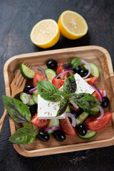 Wooden serving tray with traditional greek salad over dark brown stone surface, vertical shot, selective focus