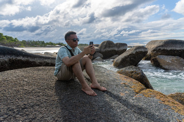 young man taking a picture from his phone in a beautiful rocky beach