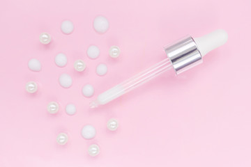 Cosmetic pipette with serum on pink background. Around - drops of serum and pearl. Stylish concept of organic essences, beauty and health products. Copy space, minimalism, flat lay. Modern apothecary.