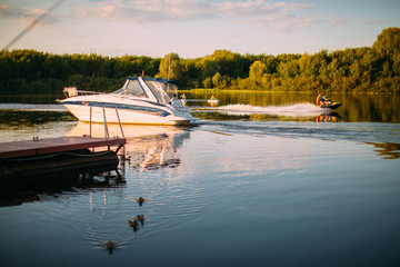 Fototapeta premium Pleasure boat sails near the pier on tranquil lake or river. Summertime landscape photography