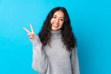 Spanish Chinese woman over isolated blue background smiling and showing victory sign