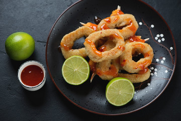 Roasted calamari rings and crab claws in panko breading served on a black plate, studio shot over black stone background