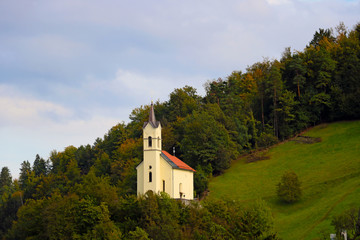 A small church high in the mountains against the backdrop of green trees.
