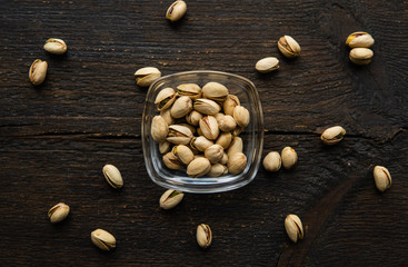 Pistachios in a small plate with scattered nuts of almonds around a plate on a vintage wooden table...