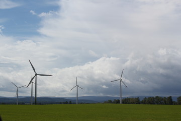wind turbines on a green field with trees and cloudy sky