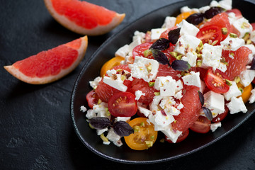 Salad with grapefruit, feta cheese, cherry tomatoes and red basil leaves on a black plate, selective focus, closeup