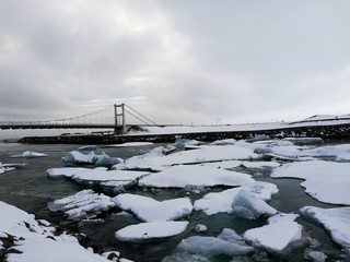  glacier lagoon in iceland with a suspension bridge in the background, chunks of ice