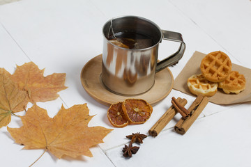 Mug of tea and waffles. Nearby are dried maple leaves, cinnamon, anise and dried oranges on the table. Autumn still life.