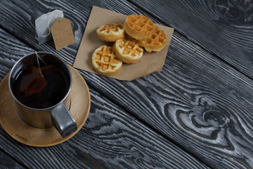 Mug of tea and waffles. Nearby is a tea bag. On painted boards. Autumn still life.