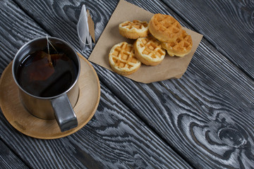 Mug of tea and waffles. Nearby is a tea bag. On painted boards. Autumn still life.