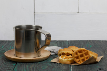Mug of tea and waffles. Nearby is a tea bag. On painted boards. Autumn still life.