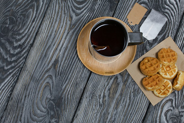 Mug of tea and waffles. Nearby is a tea bag. On painted boards. Autumn still life. Shot from above.