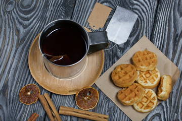Mug of tea and waffles. Nearby is a bag of tea and spices. On painted boards. Autumn still life.