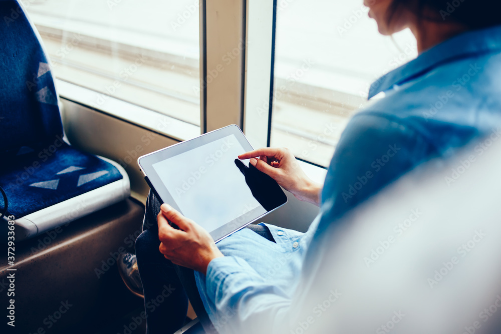 Poster cropped image of female choosing items on digital tablet while making shopping in transport, young w