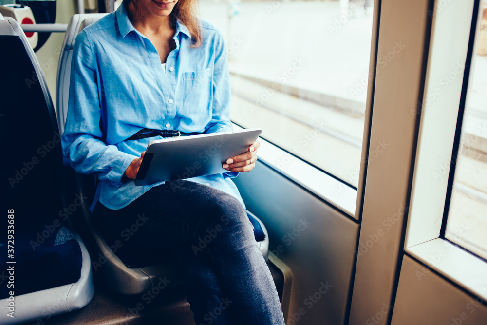 Poster cropped image of young woman using digital tablet and free wifi connection in tram while getting to 