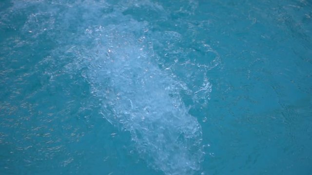 Water flow into a swimming pool in slow motion. Water splashing on blue water surface.