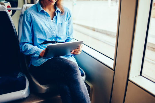 Cropped image of young woman using digital tablet and free wifi connection in tram while getting to job, female checking banking balance on portable pc typing information sitting in public transport.