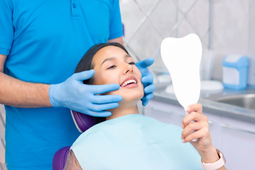 young women checks her teeth in the mirror. Young woman in the dentists office. New dental implants.
