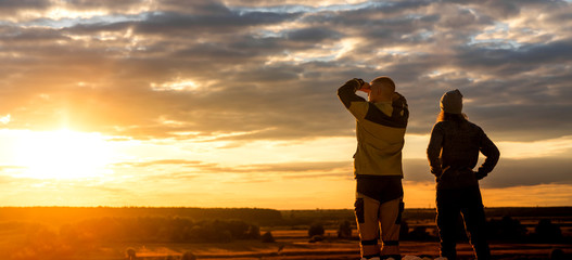 A young man with his girlfriend at sunset stand and look at the sky.