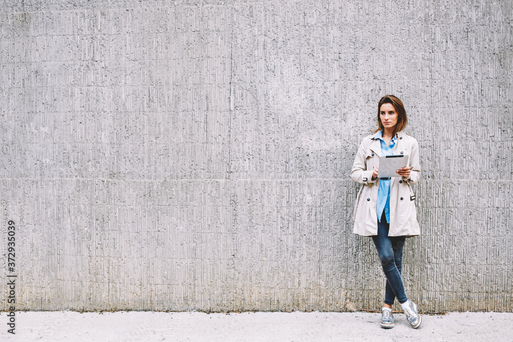 Poster thoughtful female blogger dressed in casual coat looking away while installing application via 4g in