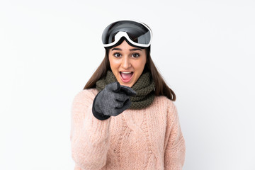 Skier girl with snowboarding glasses over isolated white wall surprised and pointing front