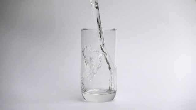 Pour water into drinking glass on white background in slow motion.