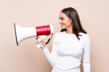 Young woman over isolated background shouting through a megaphone