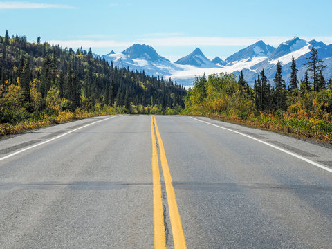 Asphalt road with yellow lines and the Worthington Glacier in Alaska in the background