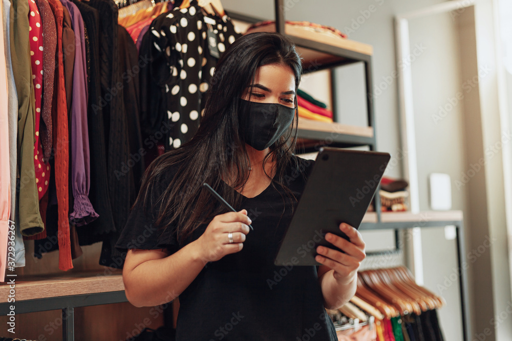 Wall mural latin woman owner of small business. entrepreneurial woman working in her clothing store. wearing fa