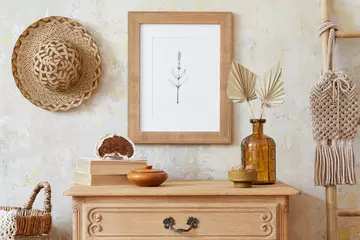 Fotobehang Boho Stylish boho interior of living room with brown mock up poster frame, elegant accessories, flowers in vase, wooden shelf and hanging rattan hut. Minimalistic concept of home decor. Template.  © FollowTheFlow
