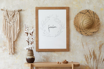 Beige boho interior of living room with mock up poster frame, elegant accessories, dried flowers in vase, wooden console and hanging rattan hut in stylish home decor. © FollowTheFlow