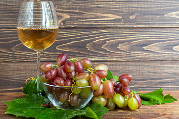 Large and light, wine grapes. It is covered with a white coating called yeast. Glasses are filled with light wine. Water drops on berries. On a wooden background.