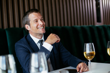  Handsome businessman dressed in the suit drinking wine. Businessman and businesswoman enjoying in the restaurant.