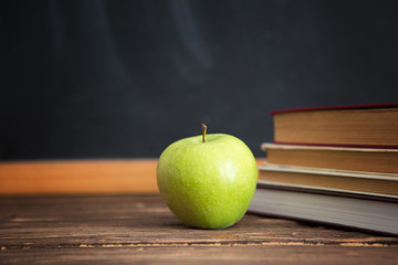Books and apples on wooden table against the background of the chalkboard or blackboard.