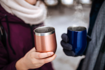 Two people hold thermo mugs with hot steaming tea