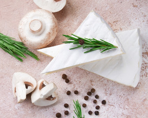 Cheese brie on a beige concrete background with rosemary, allspice and mushrooms close-up in a high...
