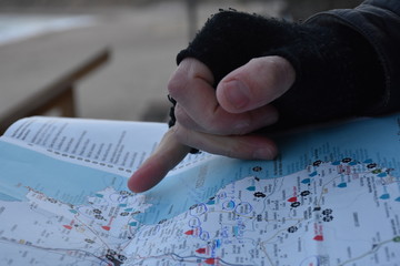 Mano con mitón señalando punto determinado en mapa turístico planificando ruta - obrazy, fototapety, plakaty