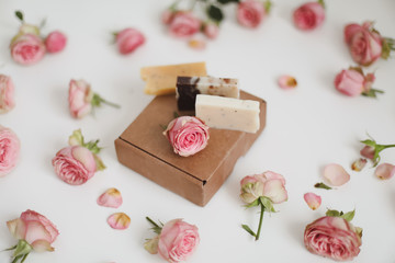 Gift box with natural homemade soap bars and rose flowers on white background. Holiday gift, opening present, top view. 