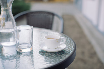 Jug, glass of water and cup of coffee on table at terrace. Outdoors, copy space.
