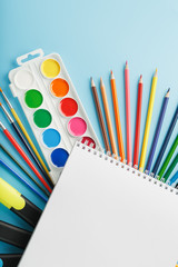 Fototapeta premium An album for drawing and creativity for school with stationery, a palette of colored paints, markers, brushes and pencils.