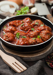 Traditional spicy meatballs in tomato sauce with pepper, garlic and parsley with onion and utensils.