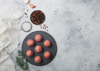 Fresh raw minced beef meatballs on round stone board with pepper, salt and garlic on light background with dill and towel.